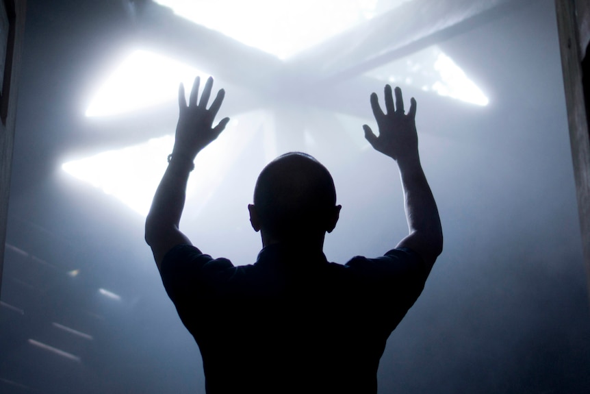 A silhouette of a man with raised hands faces light coming from above.