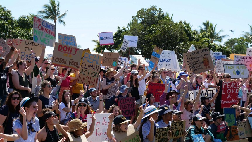 A crowd of people, including school children, holding up placards at a climate protests.