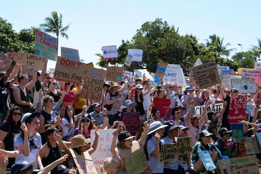 A crowd of people, including school children, holding up placards at a climate protests.