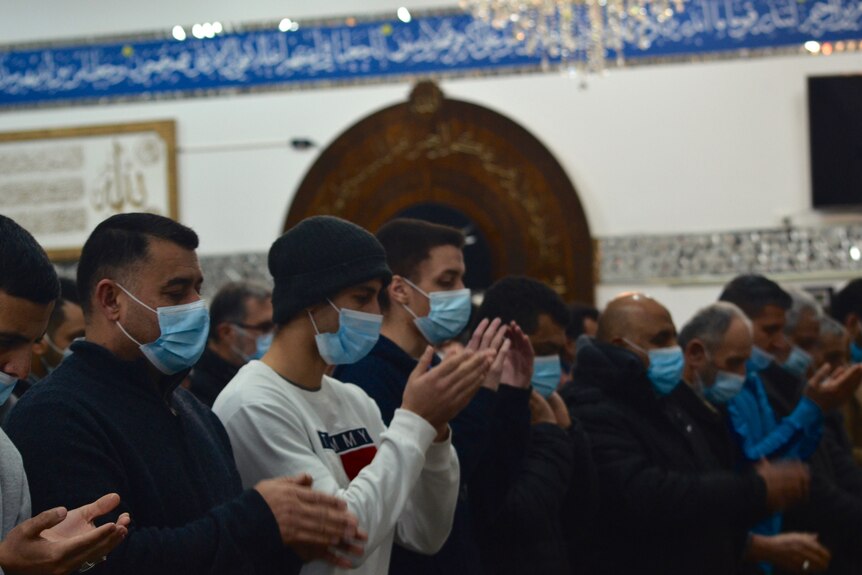Men wearing masks, standing shoulder to shoulder praying at the Ahul Bait mosque.