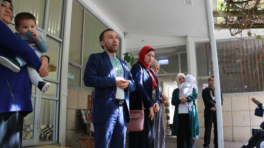 Uyghur community leader Nurmuhammad Majid standing with a group of people outside of a building.