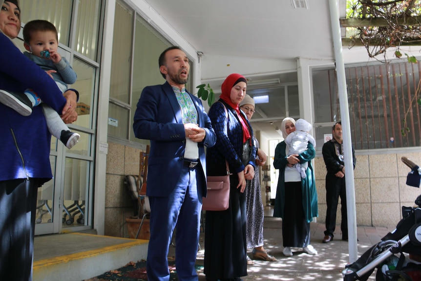 Uyghur community leader Nurmuhammad Majid standing with a group of people outside of a building.