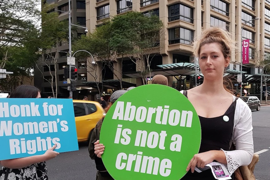 Sybil Irvin 于 2018 年 6 月 26 日在布里斯班市举行的支持堕胎的集会上举着‘堕胎不是犯罪’的标语。” class=