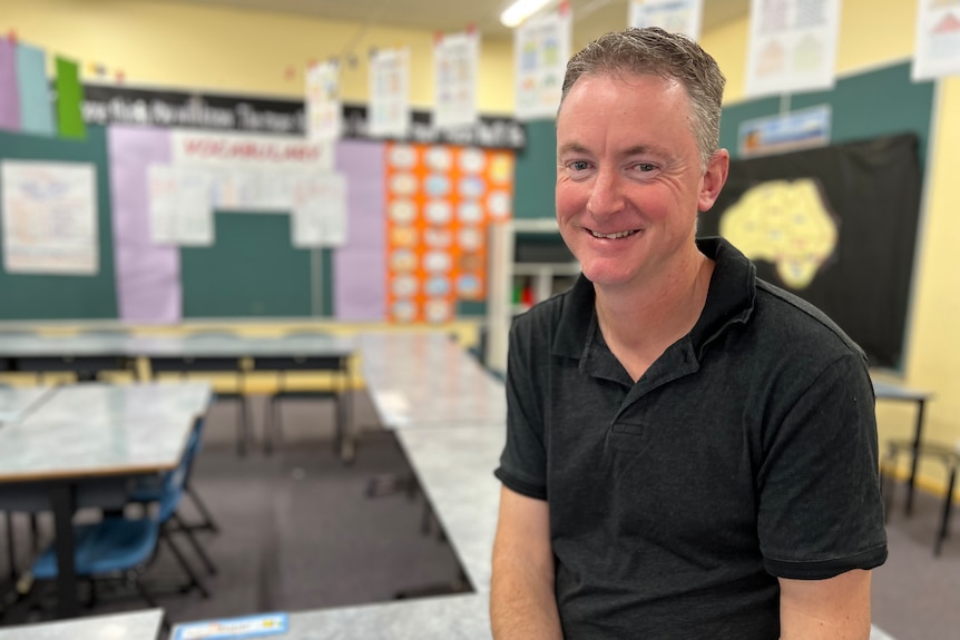 A happy man sits in an empty primary school class room