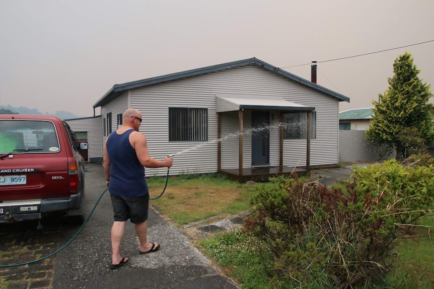 Sam Jordan sprays the front lawn of his Zeehan home with a hose.