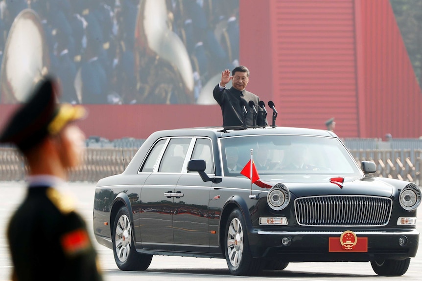 Xi Jinping waves from a black vehicle as it drives through a parade of some 15,000 troops.