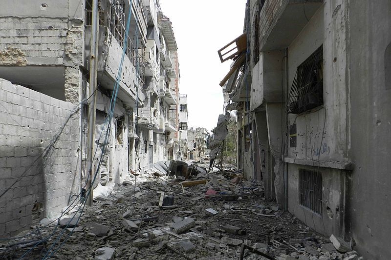 Apartment blocks are almost completely destroyed, with bricks and furniture strewn across the street.