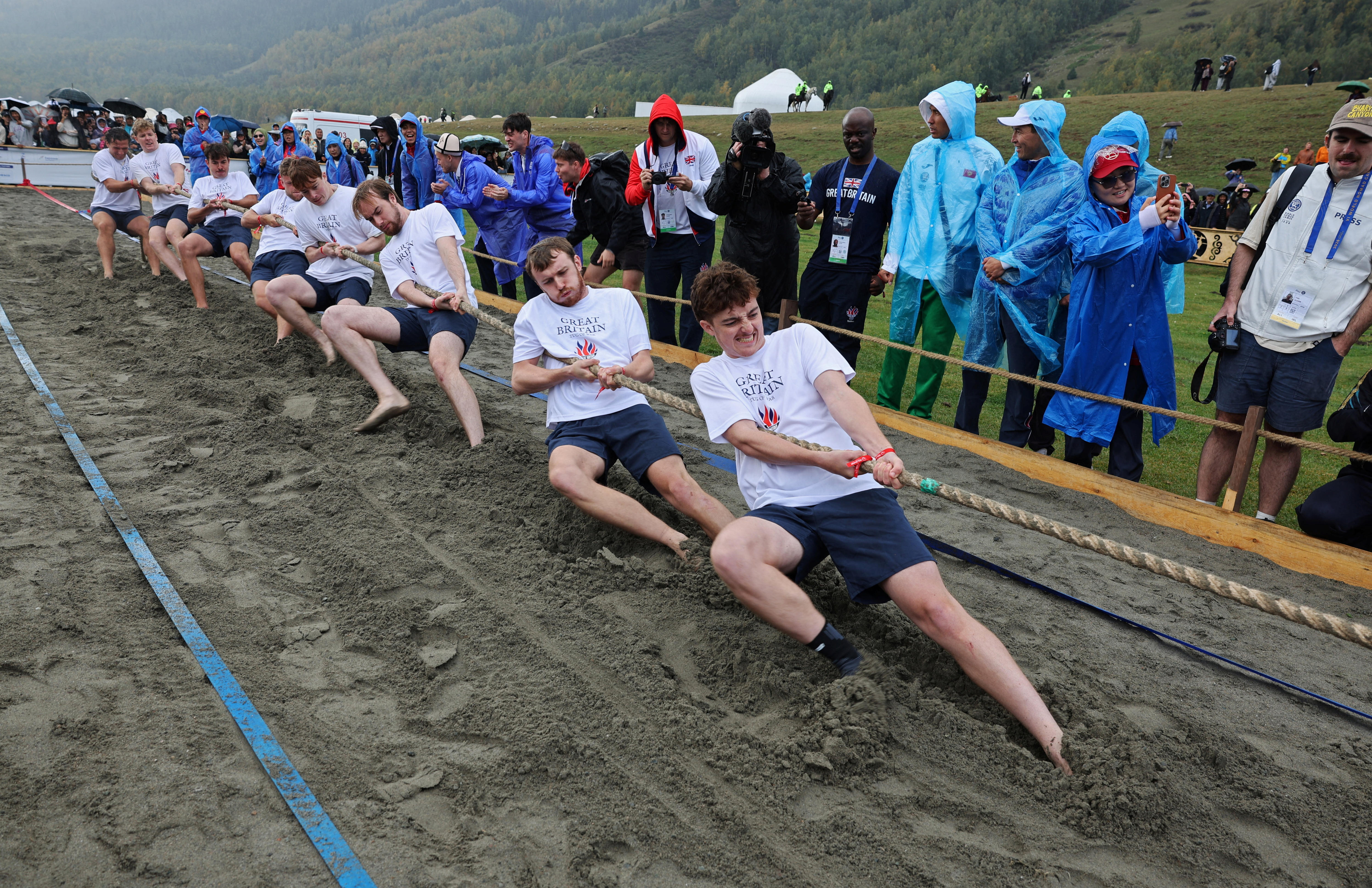 men heave into mud, pulling a rope.