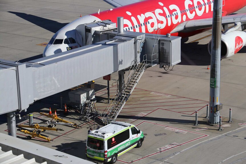 An AirAsia plane docked at an airport with an ambulance parked next to it.