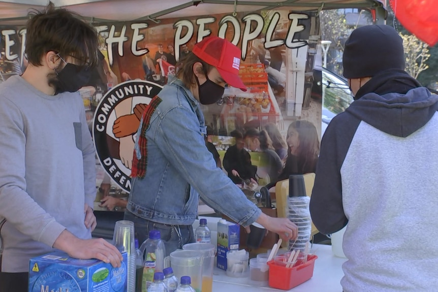 Two men wearing face masks serve food to another man