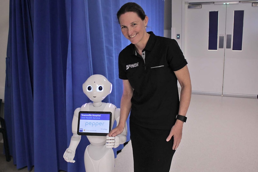 A woman holds the hand of a humanoid robot as it walks through the corridors of a hospital.