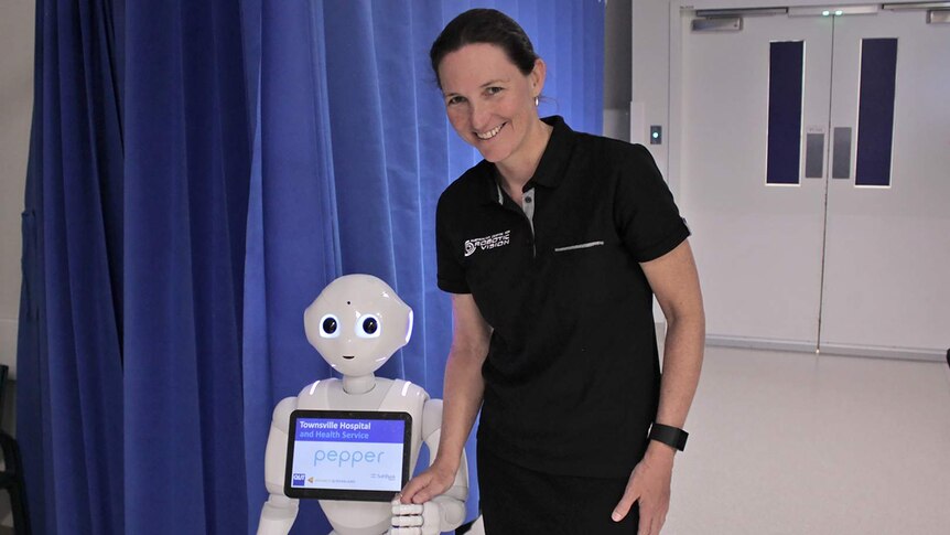 A woman holds the hand of a humanoid robot as it walks through the corridors of a hospital.