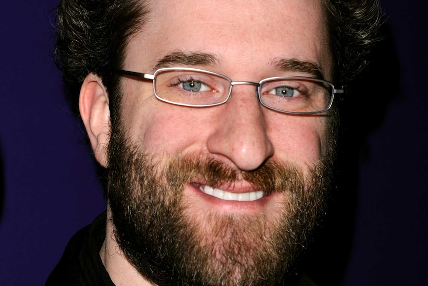 Man with curly brown hair and beard, small silver glasses