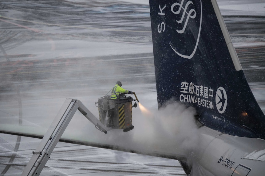 An airport worker defrosts the tail of a Chinese airplane.
