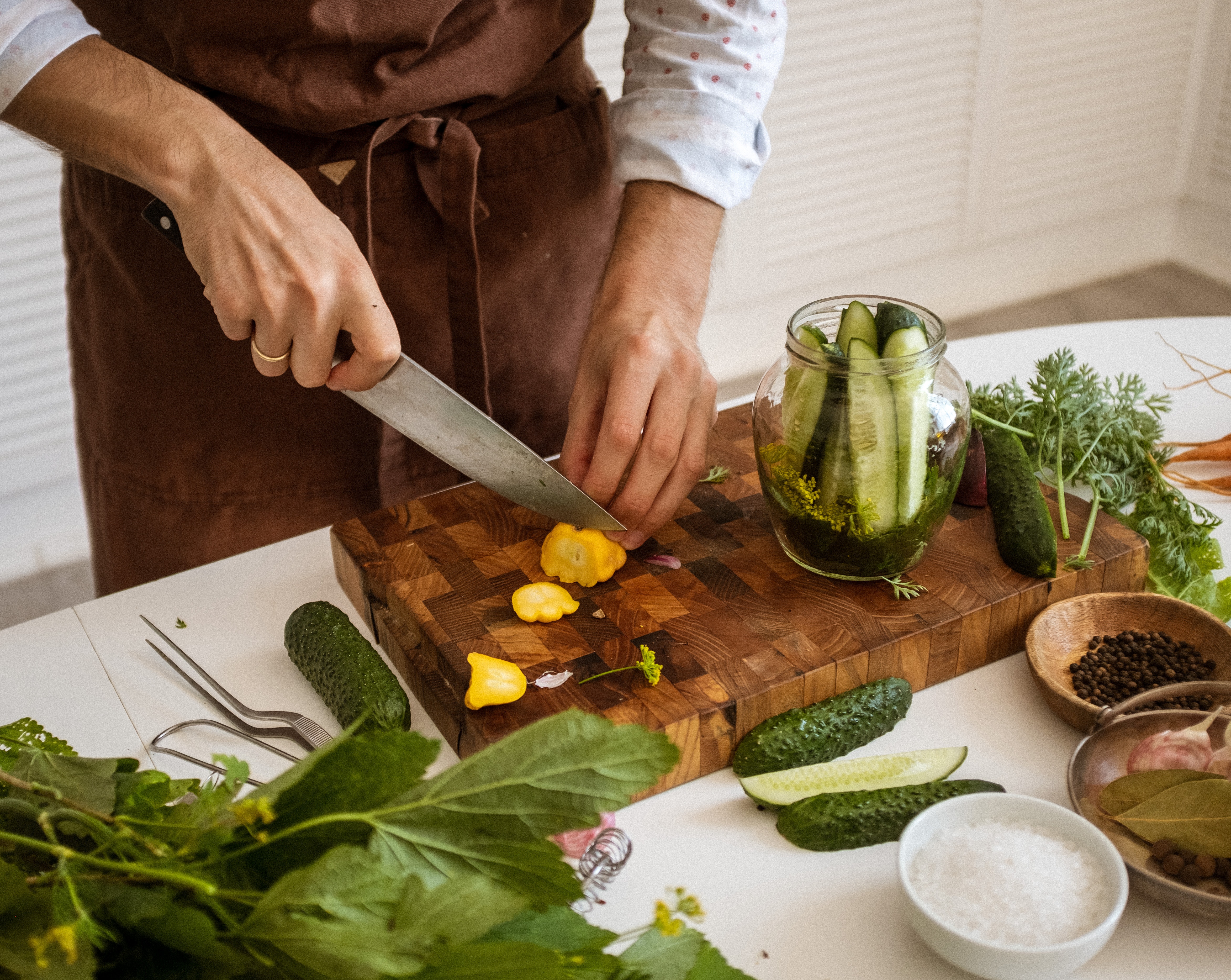 Woman cutting vegetables next to a jar of preserved pickles