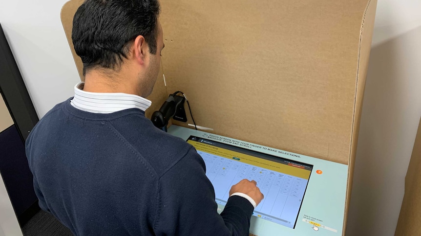 A man taps a touchscreen surrounded by a cardboard box.