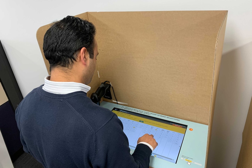 A man taps a touchscreen surrounded by a cardboard box.