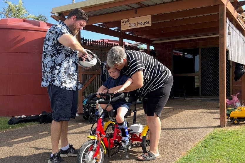 Parents strap their son into a supported bike.