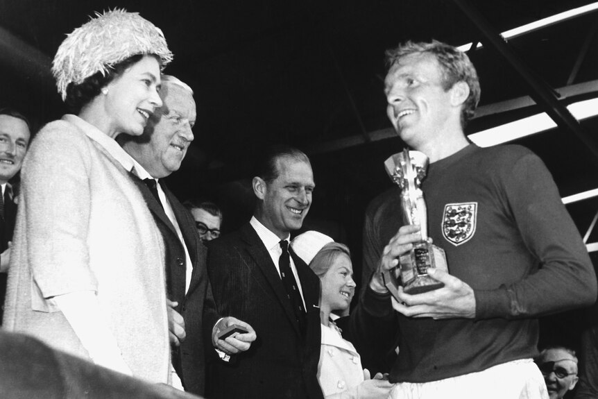 Bobby Moore holds the World Cup trophy in front of the Queen