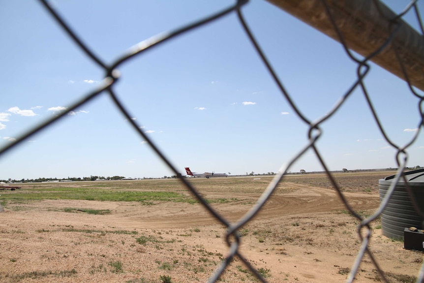 A shot of a propeller passenger plane on an outback airport runway taken through a wire fence.