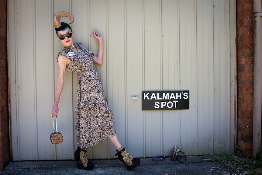 A woman with a rams horn on her head leans back at an angle so you can see her high heels