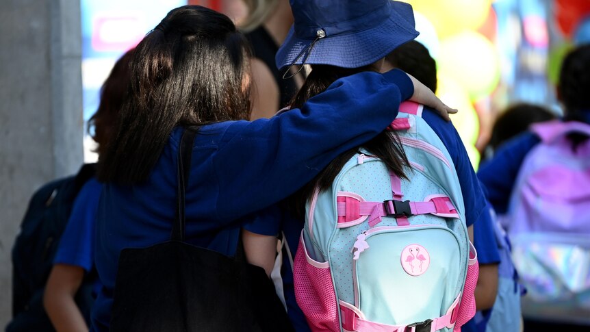 students wearing backpacks hugging each other