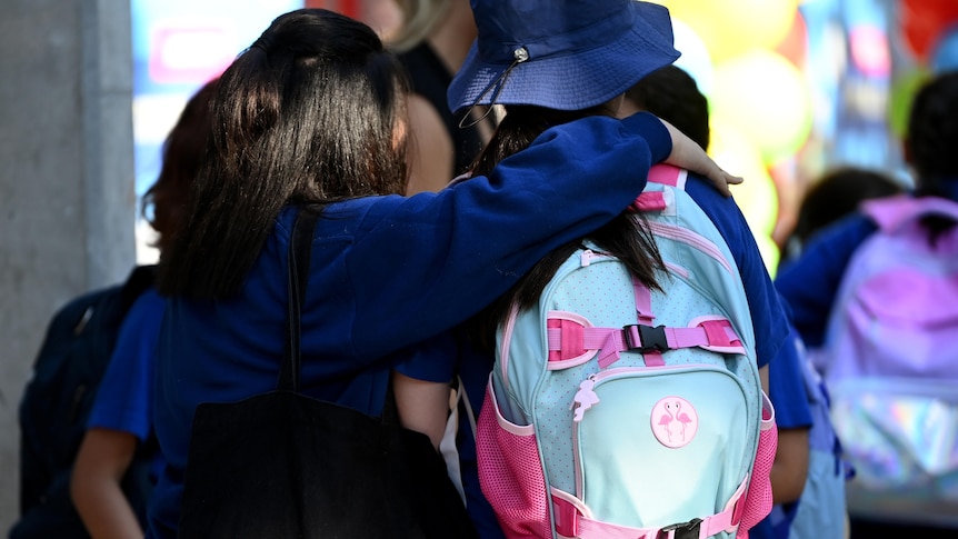 students wearing backpacks hugging each other