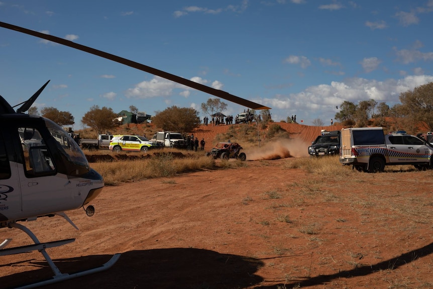 A helicopter sits on the red road, near a police car, at the scene of an accident at the Finke Desert Race.