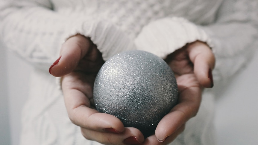 A woman holds a silver Christmas bauble.