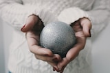 A woman holds a silver Christmas bauble.