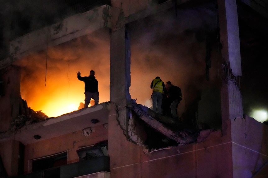 People standing inside an apartment with flames visible on the inside. 