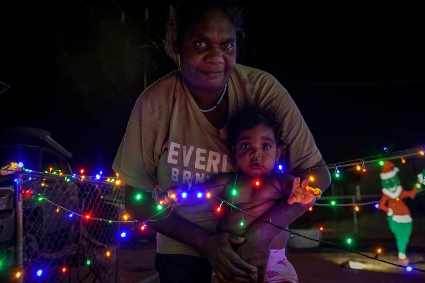 A woman holding a young child around christmas lights