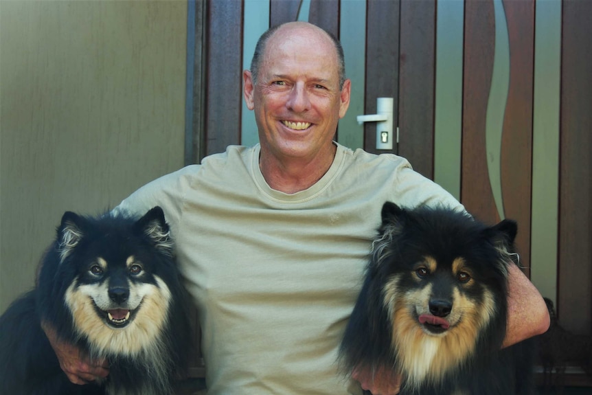 Luke Simpkins sits on steps with his two dogs, Karhu and Suvi