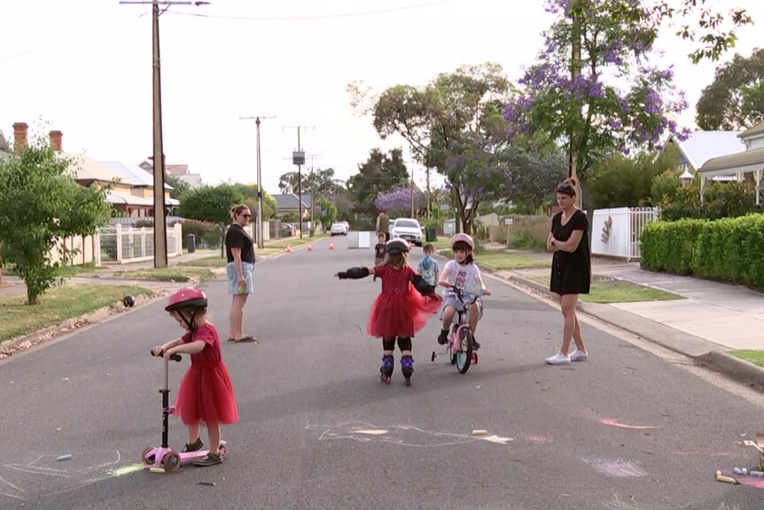 Children on scooters and bikes while two adult watch on