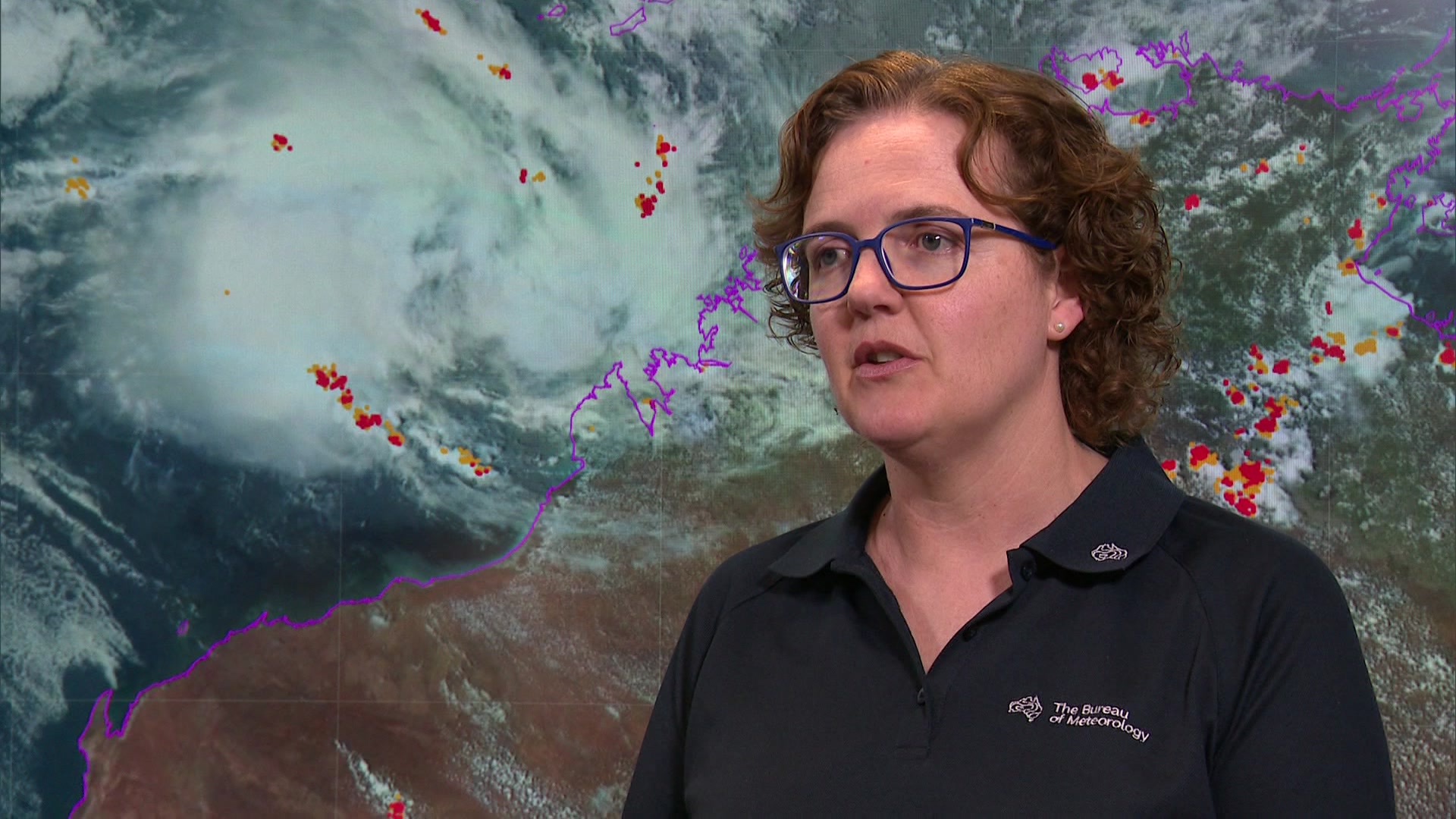 Uma mulher está em frente a um gráfico que mostra um ciclone se formando no norte de WA.