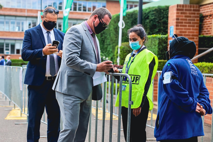 Two men holding mobile phones check in to Royal Randwick racecourse