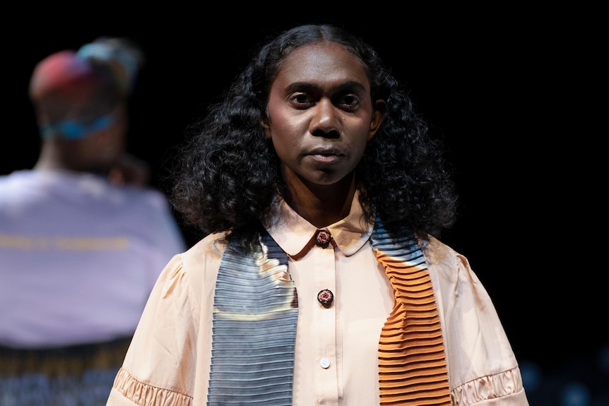 A woman wearing a colorful scarf is looking at the camera on a black background. 