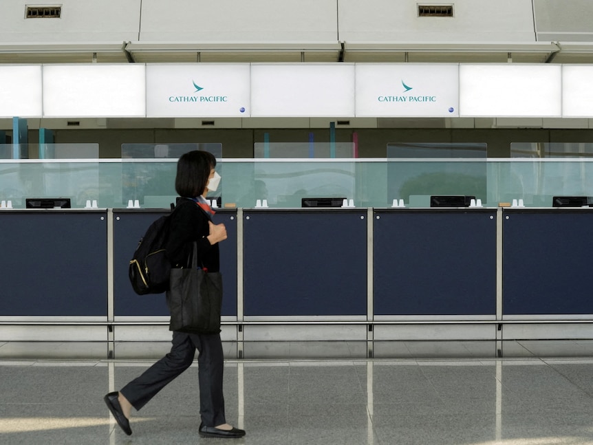 A woman wearing a mask walks past empty counters in the airport. 