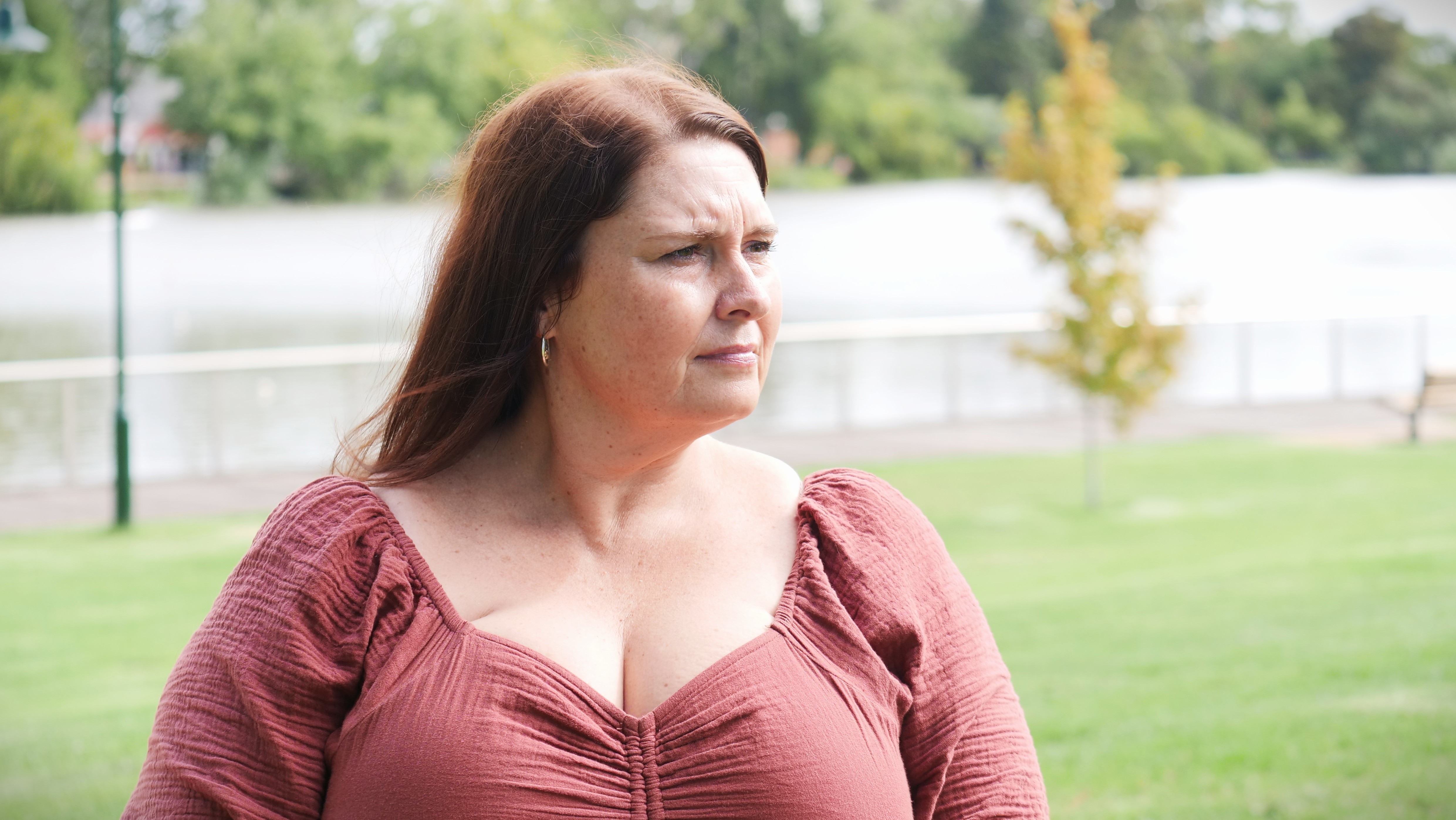 A woman in a pink top looks into the distance.