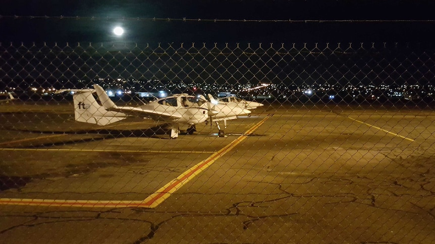 Light aircraft parked on the tarmac under moonlight.