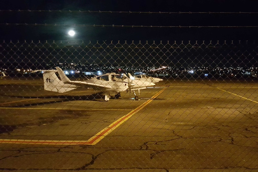 Light aircraft parked on the tarmac under moonlight.