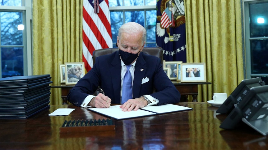 US President Joe Biden signs executive orders in the Oval Office.