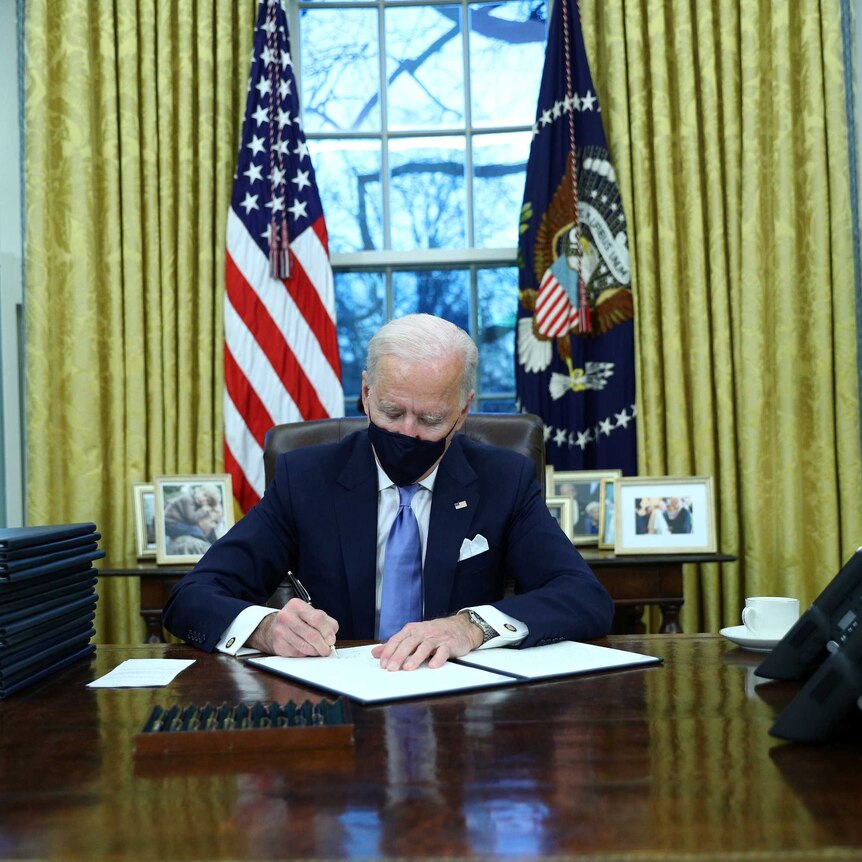 US President Joe Biden signs executive orders in the Oval Office.