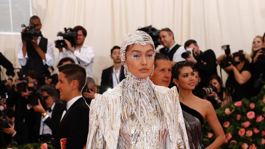 Hadid wears a sequin body suit, complete with cape and cap