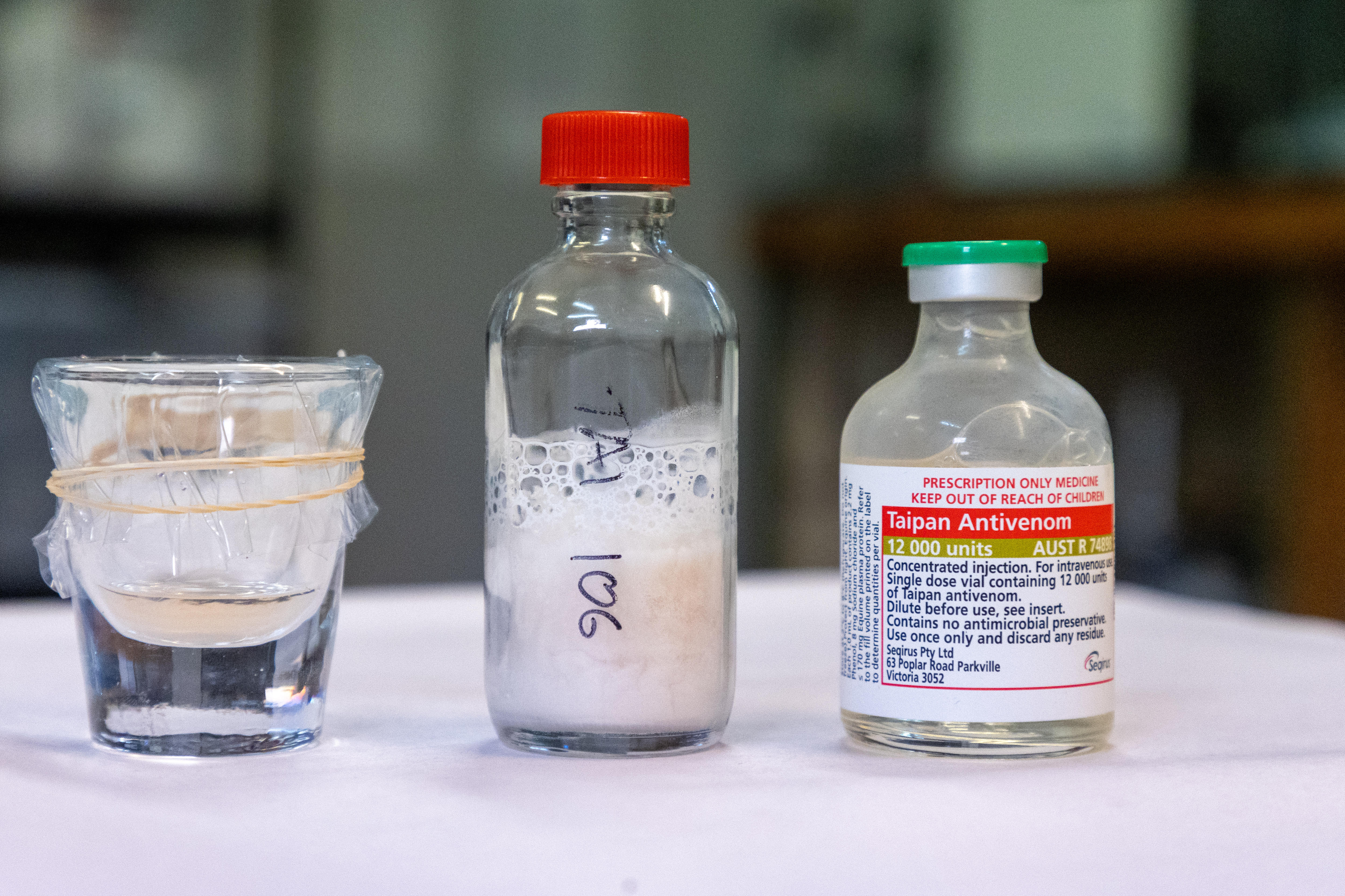 Sobre una mesa hay un vaso de chupito con un líquido transparente y dos botellas con un líquido lechoso.