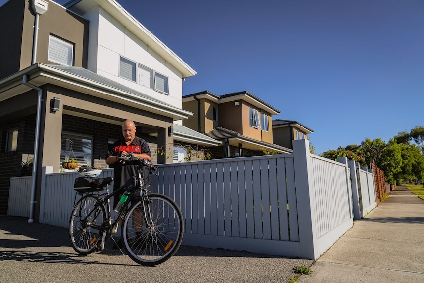 Danny stands with his bike, in the front of a grey and white townhouse