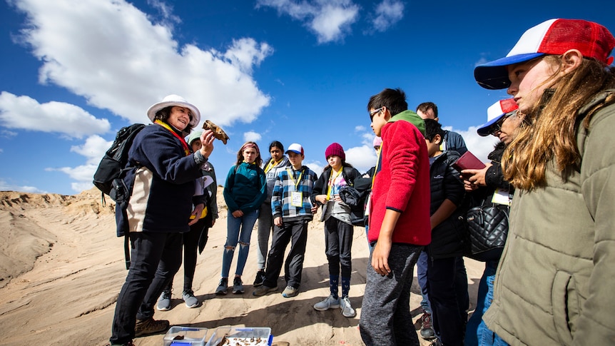 Scientist Dr Nicola Stern holds a fossil in front of her face while school students look on at Lake Mungo.
