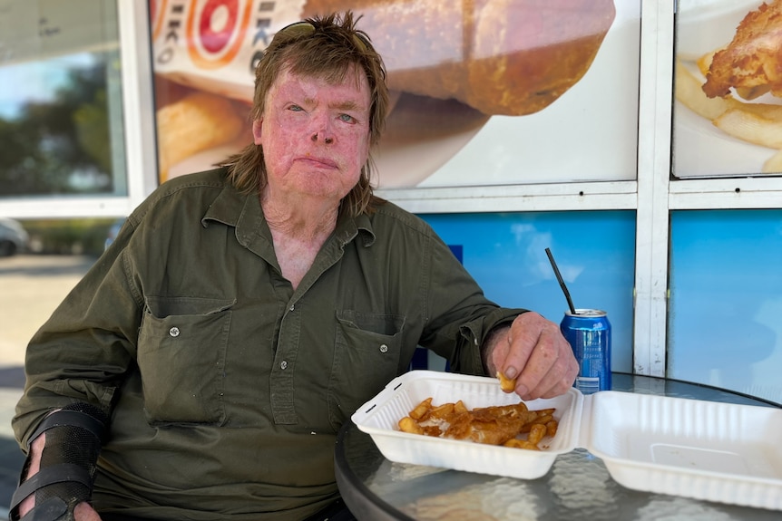 A man sits at a cafe table, eating fish and chips.