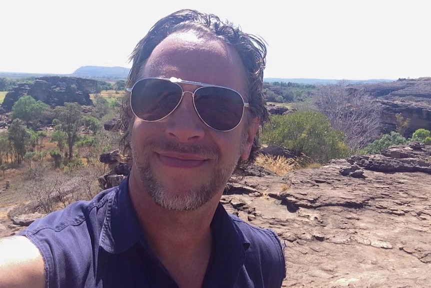 James Dunlevie wears sunglasses and smiles into the camera while hiking in the NT.