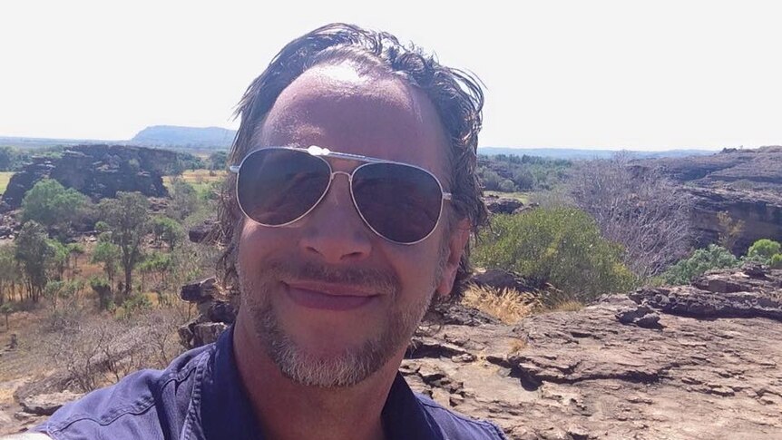 James Dunlevie wears sunglasses and smiles into the camera while hiking in the NT.